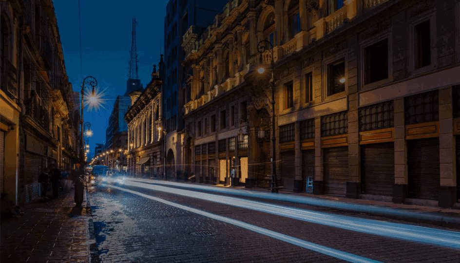 A bustling street in Mexico City at night, with illuminated buildings, and car headlights creating streaks of light