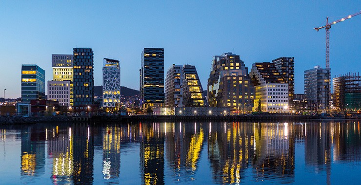 A beautiful image of the Oslo waterfront at night, featuring a row of modern skyscrapers illuminated against a dark sky